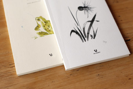 Detalle de dos libros con cubierta verjurado: uno en acabado crema y el otro en acabado blanco.