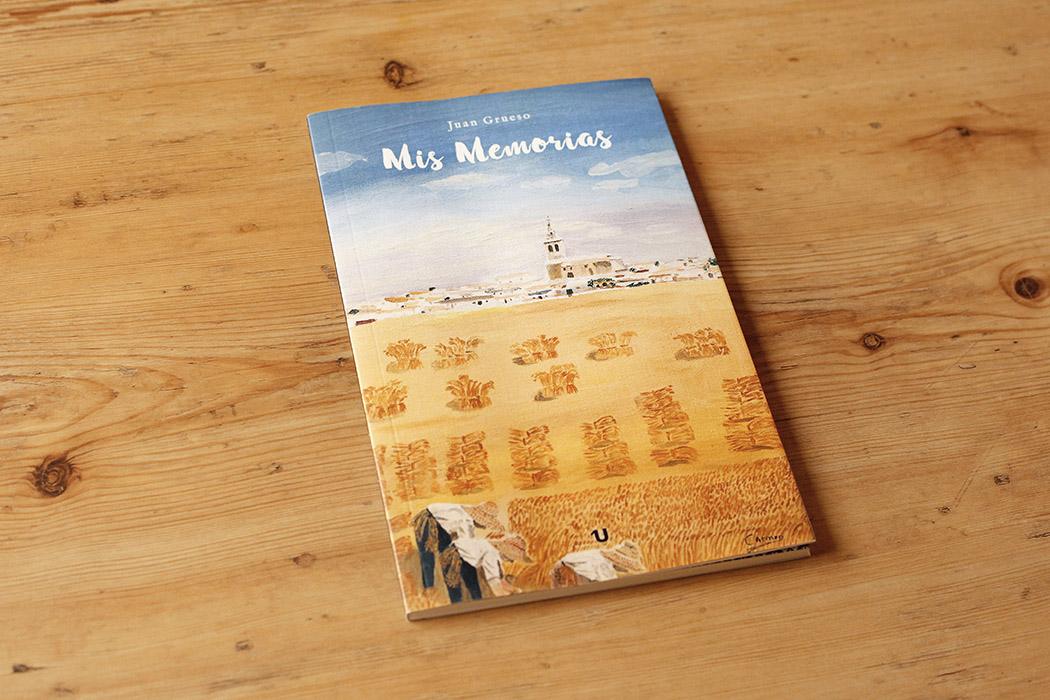 Foto de la portada del libro "Mis memorias", obra de Juan Grueso. La portada es una ilustración de un campo de trigo en plena siega con un pueblecito al fondo, bajo el cielo azul.